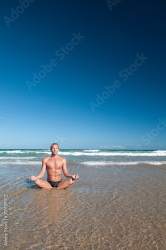 Man sitting cross-legged meditating in lotus position on the shore of a wide  tranquil beach