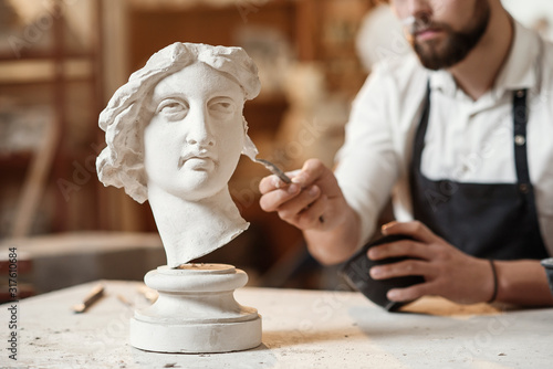 Fototapeta Skillful sculptor makes professional restauration of gypsum sculpture of woman's head at the creative workshop