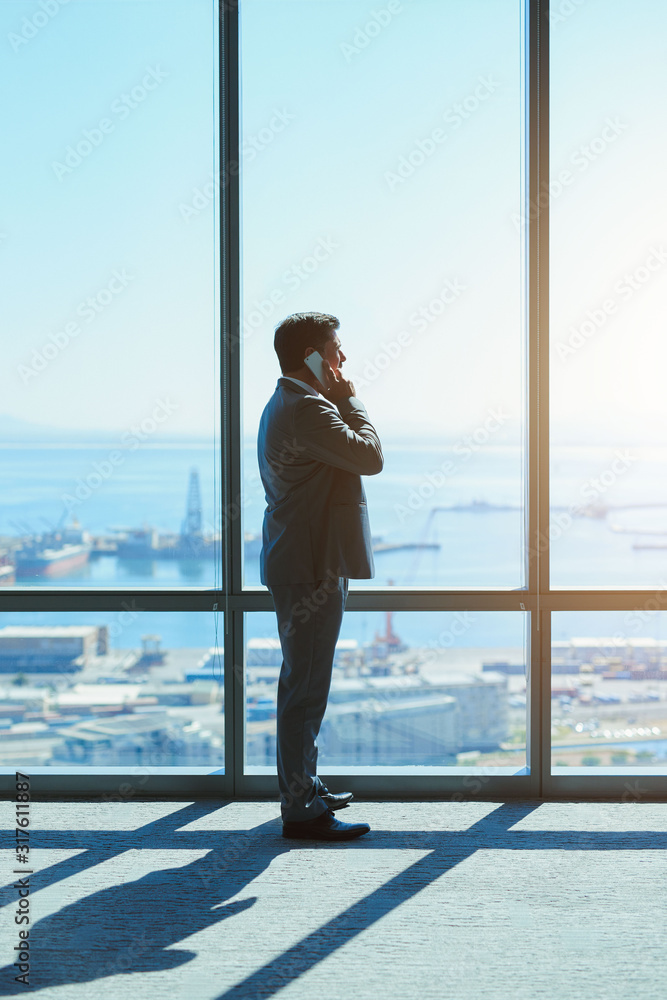 Business leader on phone at large window in top-floor office Business leader on phone at large window in top-floor office