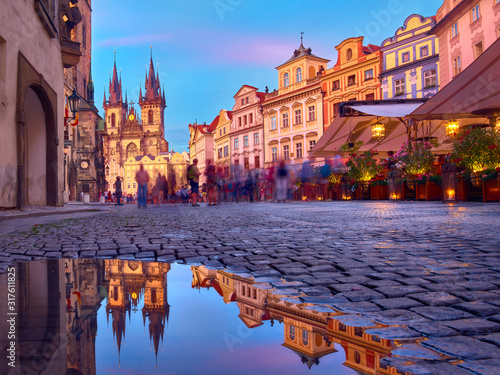St Mary Tyn Church in Prague with reflection in a pool of water after Summer rain with tourists walking by towards Old Town Square. Romantic Prague, travel background at sunset.