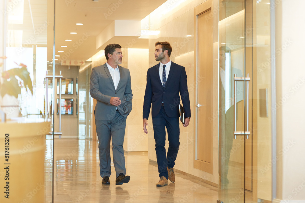 Mature businessman walking and talking with young colleague Mature businessman walking and talking with young colleague