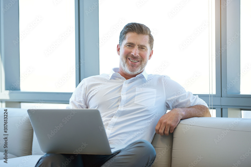 Mature man sitting with laptop on a couch smiling Mature man sitting with laptop on a couch smiling