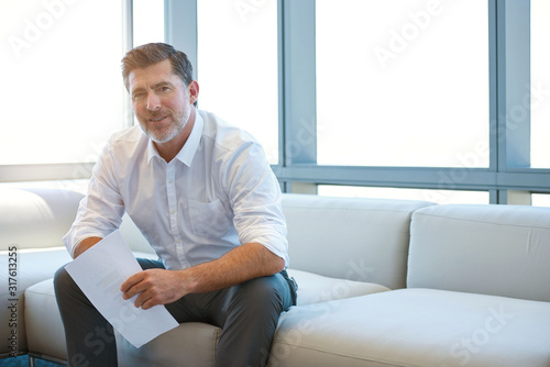 Mature business entrepreneur sitting on couch with paperwork smiling