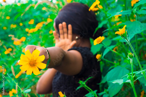 shy black girl holding a sunflower towards the camera covering her face