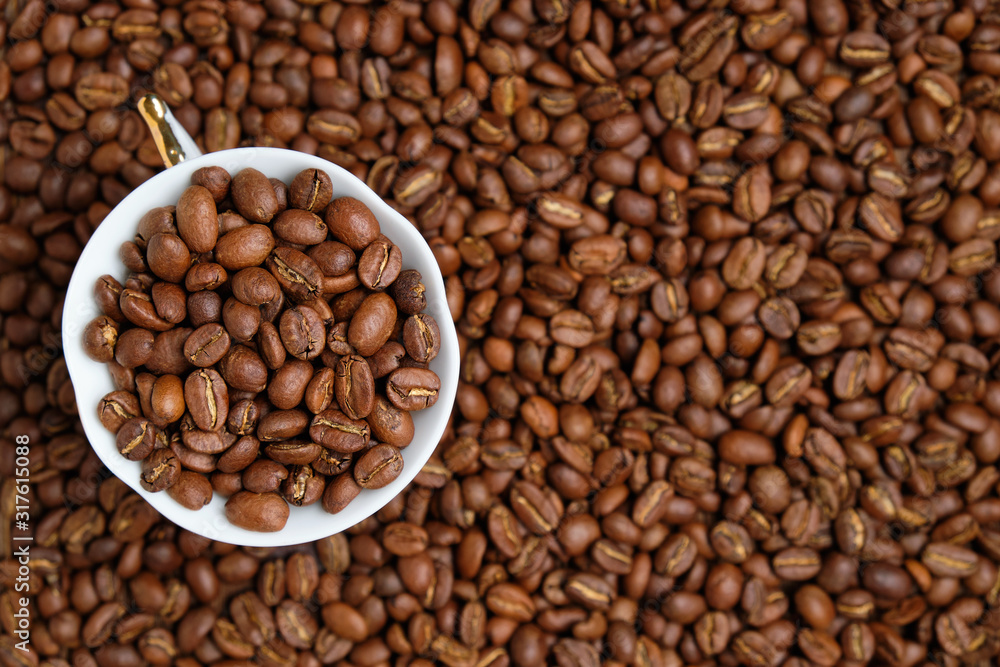 Fototapeta premium A white cup is peppered with beans against the background of coffee beans. Copy space. Top view.