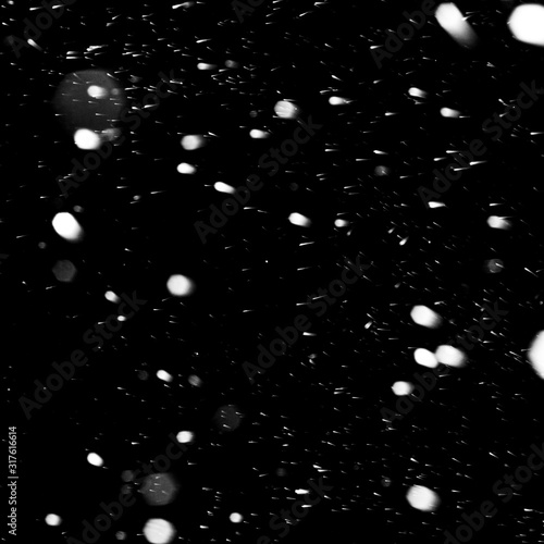 flakes of snow falling fast against a black sky, the front and background blurred with a bokeh effect