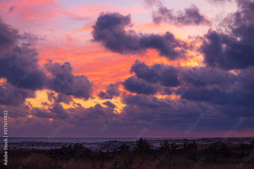 Obraz premium Vibrant sunset colors within ominous storm clouds moving over a beach. Long Island New York 