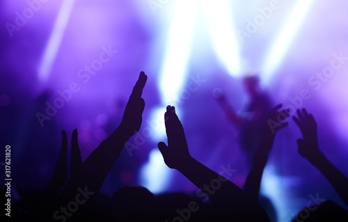 Audience with hands raised at a music festival and lights streaming down from above the stage. Crowd raising their hands, dancing and enjoying great the concert.