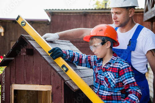 The boy holds the building level, checking the accuracy of the dog house roof. photo