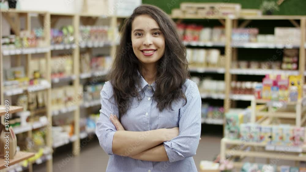 Pretty caucasian girl in supermarket background standing with her arms crossed, smiling broadly at camera, enjoying successful lifestyle. Pretty caucasian girl in supermarket background standing with her arms crossed, smiling broadly at camera, enjoying successful lifestyle.