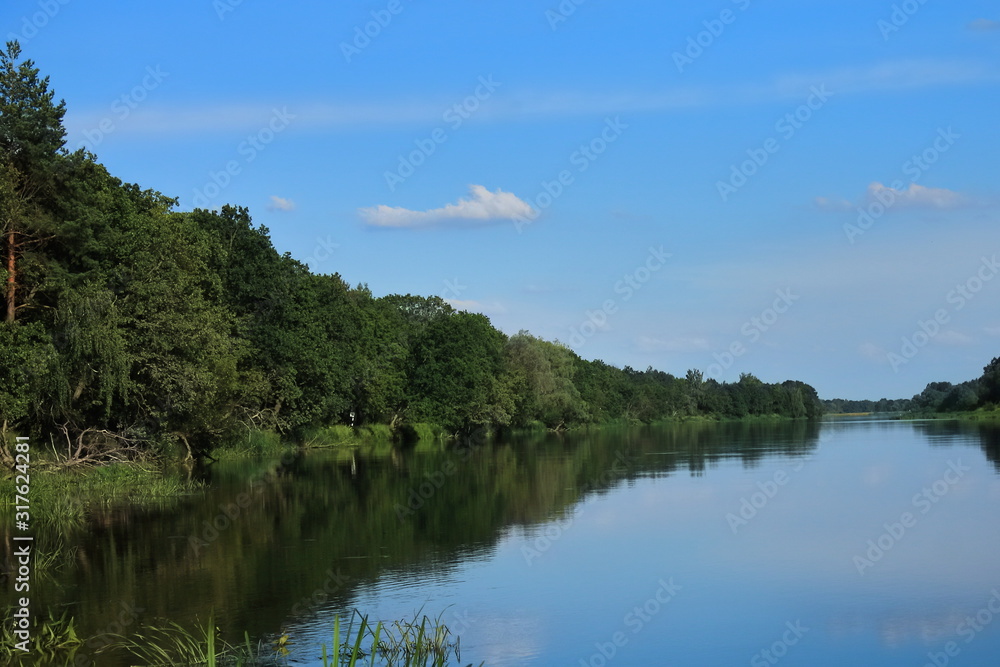 Big beautiful river, blue sky in summer, forested banks against the blue sky. European Sunny summer. Rest on the river Bank in a tent.
