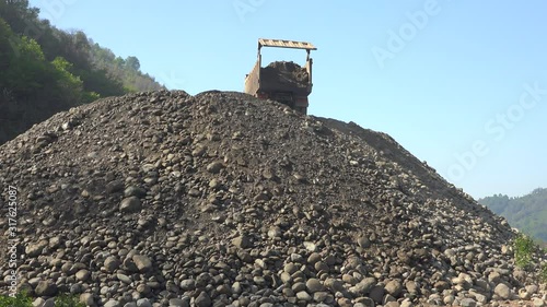Large big road material. Vehicle doing back maneuver. Dump truck unloading sand and gravel mix. Broken shredded river bed stone. Lift damper transporting transport tipper old dirt stack mass stacking.