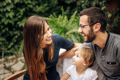 Family enjoying with their daughter in the garden. Pretty blonde little girl in the garden sitting between her young parents. Love and family concept.