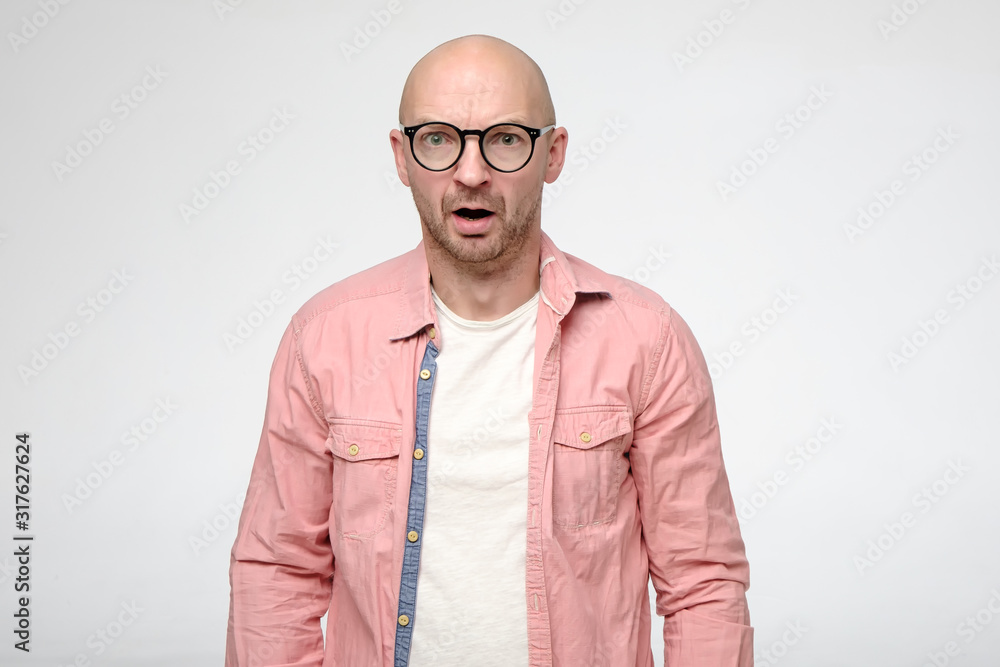 Shocked, upset bald man with glasses in a stupor, emotionally opened mouth and stares at the camera in disbelief. Shocked, upset bald man with glasses in a stupor, emotionally opened mouth and stares at the camera in disbelief.