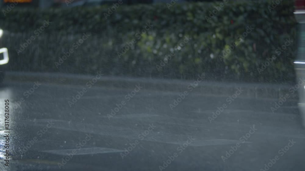 VALENCIA, SPAIN - OCTOBER 22, 2019: Pouring rain and cars passing by splashing rainwater on the road. Nasty dull evening in the city