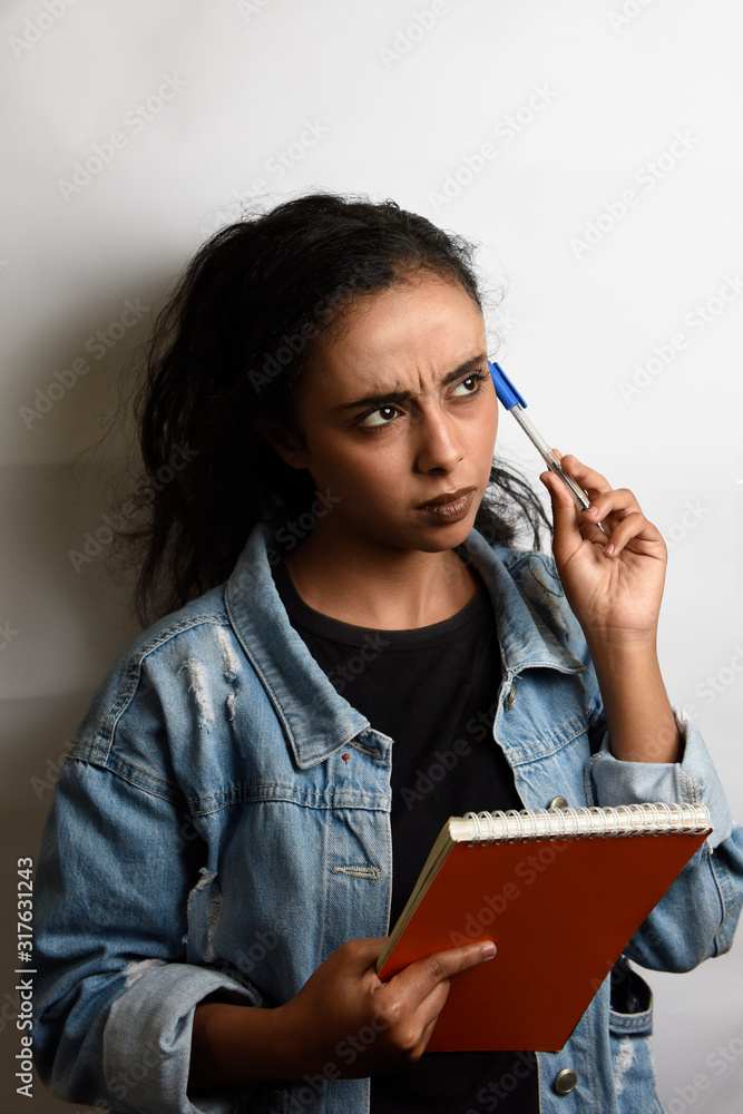 middle eastern student girl holds open book looking up puts pencil on cheek thinking on a white background. middle eastern student girl holds open book looking up puts pencil on cheek thinking on a white background.