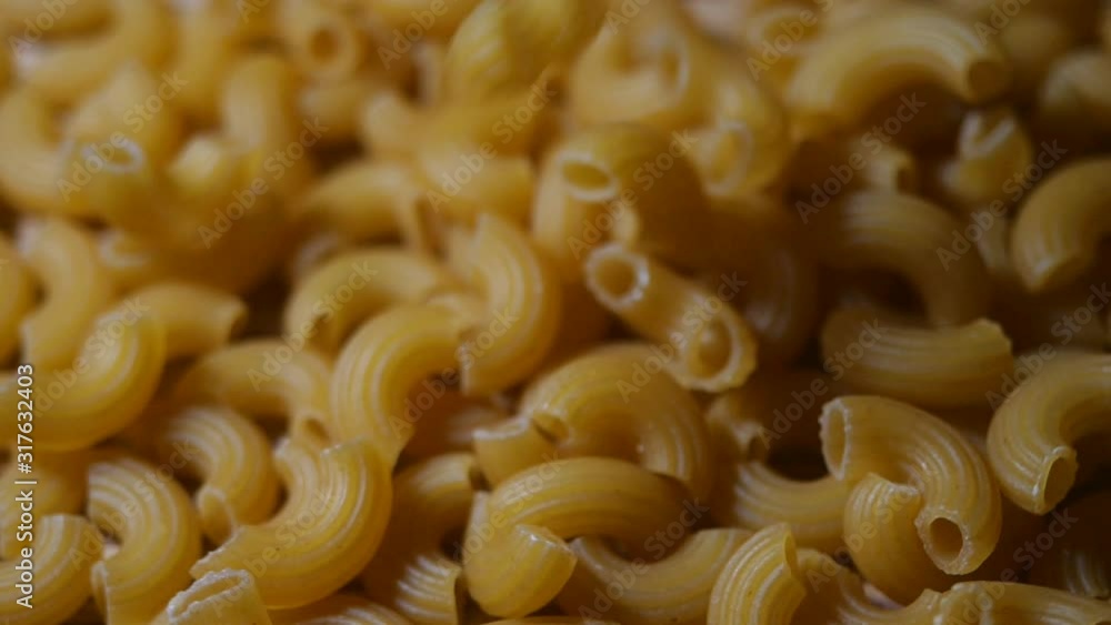 Raw macaroni falling in slow motion. Close-up elbow macaroni. Italian cuisine concept. Raw macaroni falling in slow motion. Close-up elbow macaroni. Italian cuisine concept.