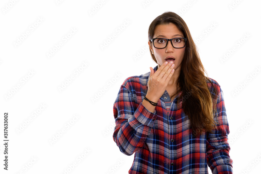 Studio shot of young beautiful woman looking surprised while covering mouth Studio shot of young beautiful woman looking surprised while covering mouth