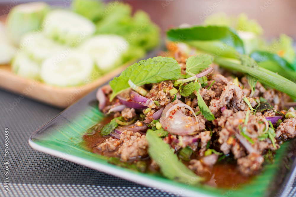 Spicy minced meat salad with blurred cucumbers background, Thai menu Spicy minced meat salad with blurred cucumbers background, Thai menu