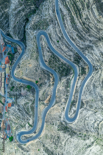 Aerial top down panorama view of a long serpentine curving road going up the hill from the bottom riverbed of the Jucar with dozens of sharp turns drawing an interesting pattern