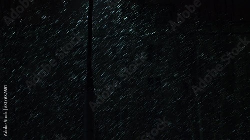 Night street with lanterns and luminous window in building opposite. Snowflakes falling in light of lantern. Luminous lettering, traffic lights, brake lights. Headlights of cars driving along street