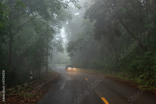 Foggy road on the mountain with a car in background.