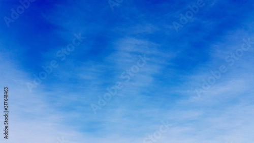 Deep blue sky backing shot with white clouds. Clean cloudscape space with just a interweave cloud to use as a background in your designing area. Royalty free stock photo.