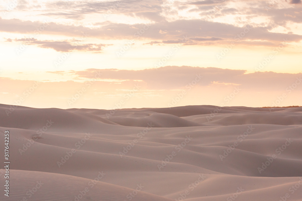 Wide boundless desert with beautiful dunes. Nothing and no one. Soft smooth shapes. Orange sky. Stockton Sand Dunes near the coast, Worimi Regional Park, Anna Bay, Australia
