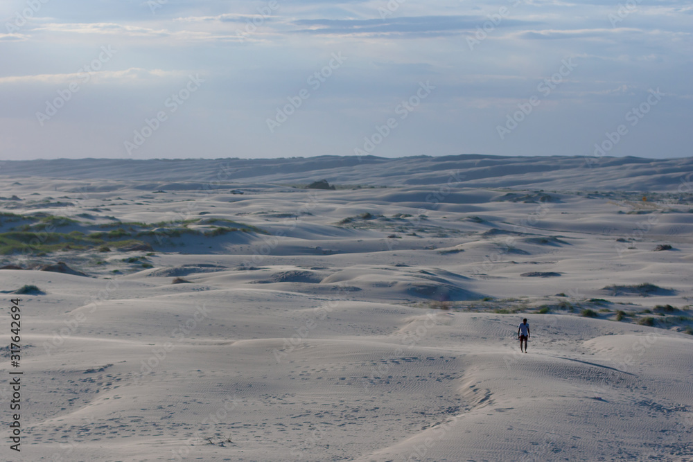 Large open desert empty space with blue sand waves. Chain tracks and a lonely man in the foreground. Stockton Sand Dunes near the coast, Worimi Regional Park, Anna Bay, Australia Large open desert empty space with blue sand waves. Chain tracks and a lonely man in the foreground. Stockton Sand Dunes near the coast, Worimi Regional Park, Anna Bay, Australia