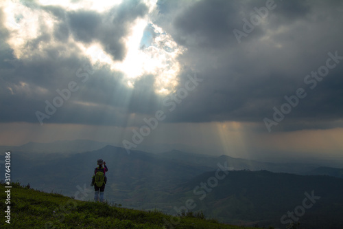woman on top of mountain with light sun in clouds