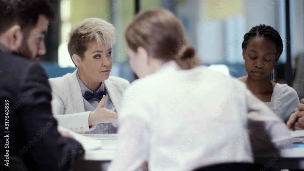 A team of young creative multi-ethnic businessmen is sitting at a table in a meeting room. Young initiative business woman gives a report on the work done. A team of young creative multi-ethnic businessmen is sitting at a table in a meeting room. Young initiative business woman gives a report on the work done.