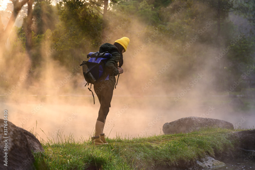 Obraz premium woman trekking alone on the lake of forest mountain with hot spring water flowing the lake in the morning, cheerfully on the move freshly morning