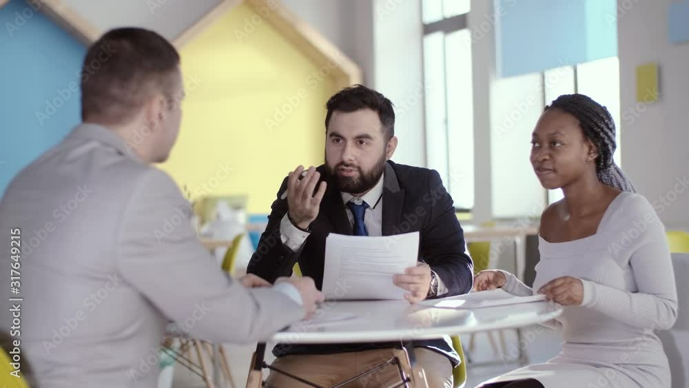 A young African American business woman at the negotiating table tells her business partner, with the help of her translator, that she agrees to the proposed conditions. Business partners shake hands. A young African American business woman at the negotiating table tells her business partner, with the help of her translator, that she agrees to the proposed conditions. Business partners shake hands.