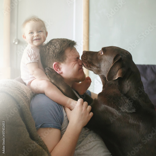 Obraz na płótnie Young caucasian father with cute smiling little baby girl sitting on his shoulders and pet labrador retriever w salonie