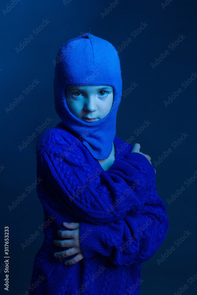Fototapeta Studio portrait of a brunette boy in a blue knitted sweater and a Balaclava-cap-mask.