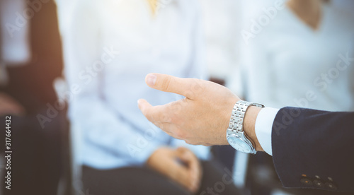 Business man making presentation to group of people in sunny office. Speaker delivering a seminar to his colleagues or business training. Teamwork and coaching concept