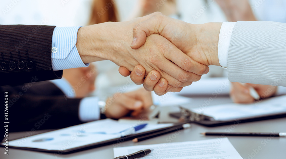Business people shaking hands at meeting while theirs colleagues clapping and applauding. Group of unknown businessmen and women in modern white office. Success teamwork, partnership and handshake Business people shaking hands at meeting while theirs colleagues clapping and applauding. Group of unknown businessmen and women in modern white office. Success teamwork, partnership and handshake