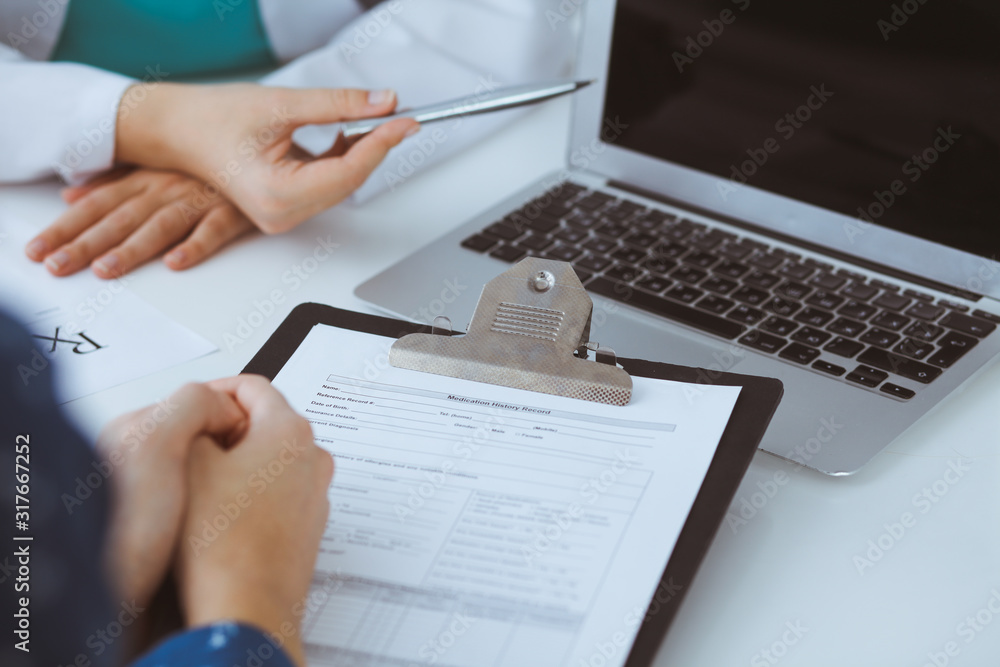 Close-up of a doctor and patient sitting at the desk while physician pointing into laptop computer. Medicine and health care concept Close-up of a doctor and patient sitting at the desk while physician pointing into laptop computer. Medicine and health care concept