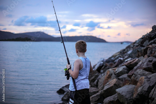 Young boy fishing off rocks at twilight
