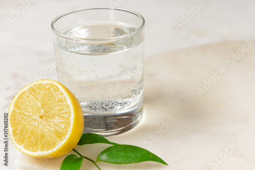 Glass of clean water and lemon on light background