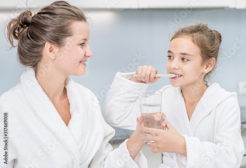 Mom gives her daughter a glass of water to rinse her mouth after brushing teeth