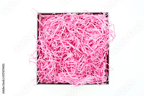 Shredded pink paper packing material in a square box. Pink spaghetti shredded packing paper used to protect fragile object while in transport. The box is isolated on white background with copy space.