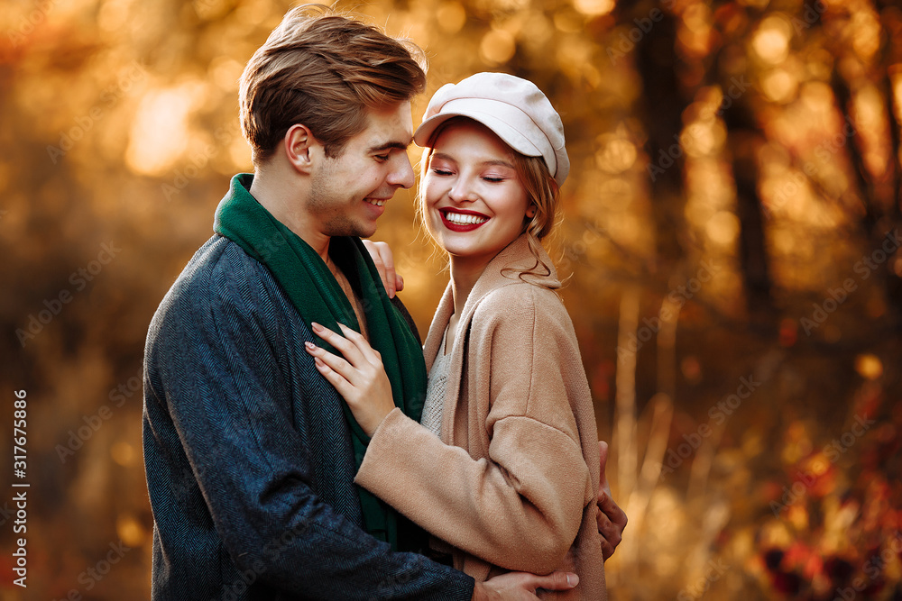 Fototapeta premium happy, couple in love hugs and smiles on the street, autumn, green scarf and cap, man and woman on a date, valentines day. walk in the park