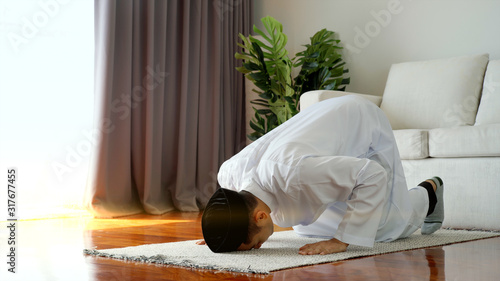 Portrait of an Asian Muslim man woman reciting Surah Al-Fatiha passage of the Qur'an in a single act of Sujud called a Sajdah or prostration in a daily prayer at home photo