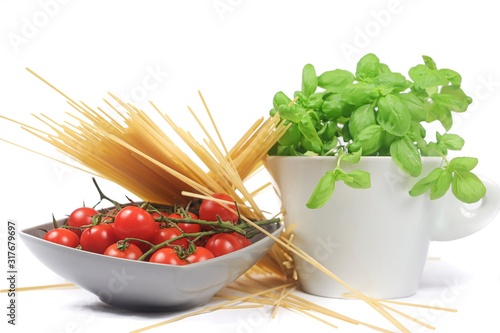 closeup of a bowl with cherry tomatoes, spaghetti and basil jar on a white background