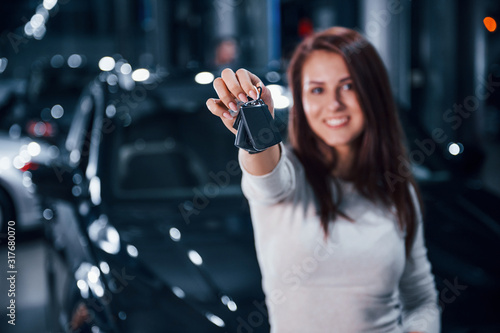 Young woman in casual clothes standing near modern black car with keys in hands
