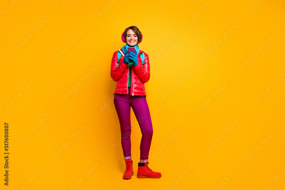 Full body photo of pretty lady walking down street using looking telephone online maps wear casual red coat boots blue scarf gloves ear covers pants isolated yellow color background Full body photo of pretty lady walking down street using looking telephone online maps wear casual red coat boots blue scarf gloves ear covers pants isolated yellow color background