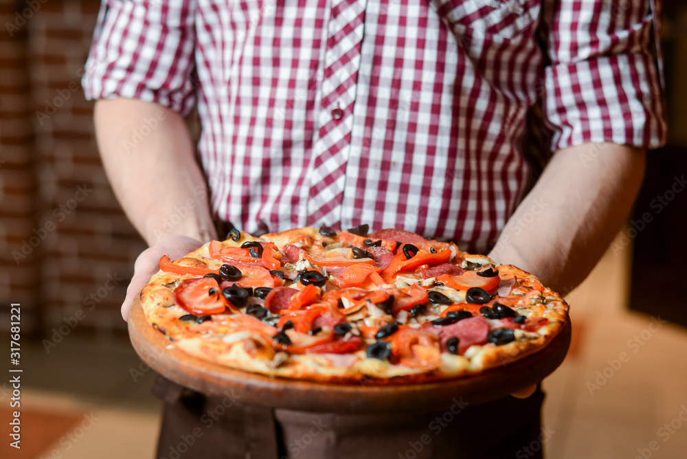A waiter holds a plate of tasty food. Italian cuisine in restaurant, Delicious pizza with spinach, olives and mushrooms
