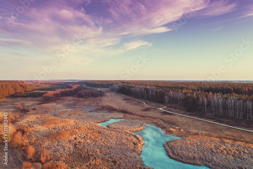 Aerial view of countryside and frozen brook in evening at sunset light. Beautiful nature landscape with cloudy sky.
