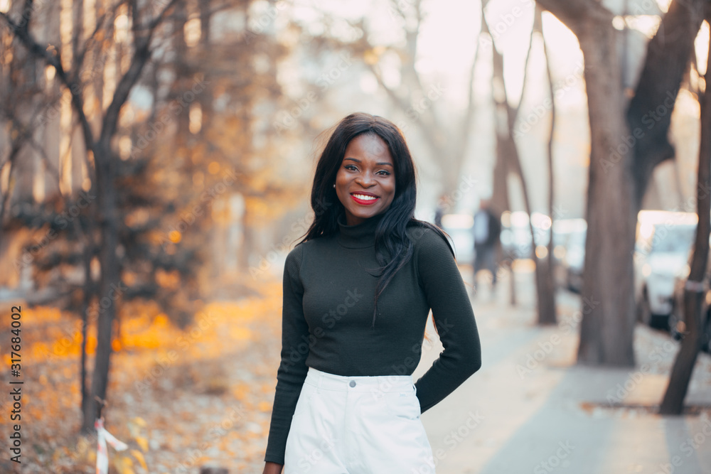 A beautiful young black African girl with a happy smile poses outdoors in the rays of the setting autumn sun. close-up. Fashion colors A beautiful young black African girl with a happy smile poses outdoors in the rays of the setting autumn sun. close-up. Fashion colors